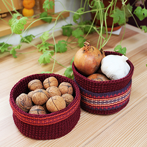 photo de deux petits paniers réalisés au crochet
				et décorés d'une bande tissée dans les tons rouges, bordeaux et oranges
