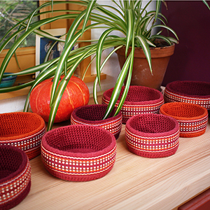 photo de plusieurs petits paniers réalisés au crochet
				et décorés d'une bande tissée dans les tons rouges et oranges