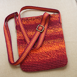 photo d'un sac réalisé au crochet avec une bandoullière 
				tissée dans les tons rouges-oranges