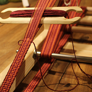 photo du tissage d'un galon dans les tons rouges 
				sur un inkle loom